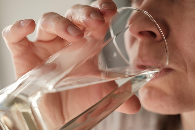 Close-up gezicht van een vrouw die vers helder water drinkt uit een glas Gezondheidsconcept