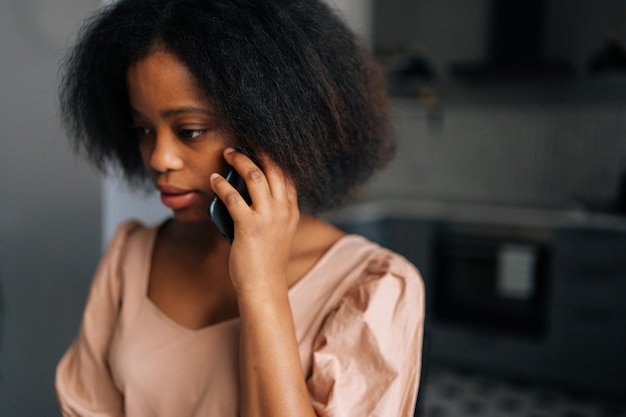 Close-up gezicht van gekrulde jonge Afro-Amerikaanse vrouw praten op mobiele telefoon thuis Close-up portret van aantrekkelijke zwarte vrouwelijke bellende smartphone binnen