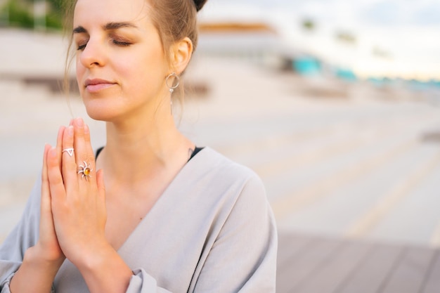 Close-up gezicht van meditatieve jonge vrouw die yoga beoefent die namaste pose uitvoert met gesloten ogen buiten in stadspark