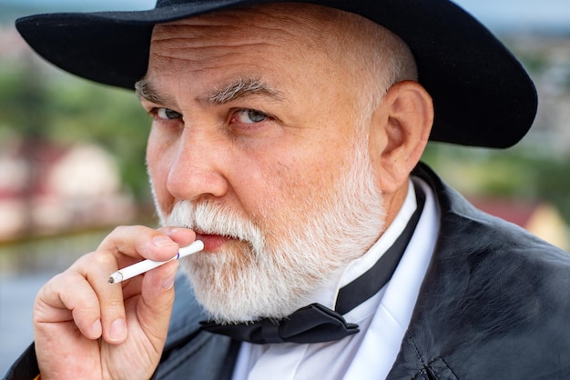 Foto close-up gezicht van serieuze stijlvolle hipster grootvader in leren jas rooken buiten ouder