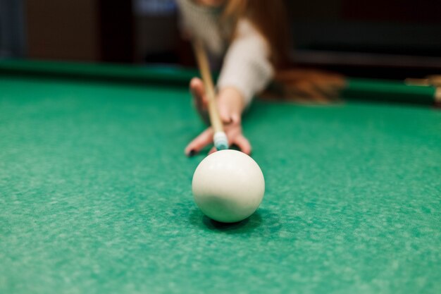 Close up at the girl aiming a cue ball on a ball in a pool table