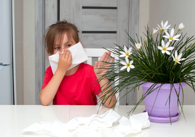 Foto primo piano della ragazza che si soffia il naso in un tovagliolo di carta a casa accanto a un fiore. allergia al polline dei fiori, la ragazza ha il naso che cola sulle piante d'appartamento.