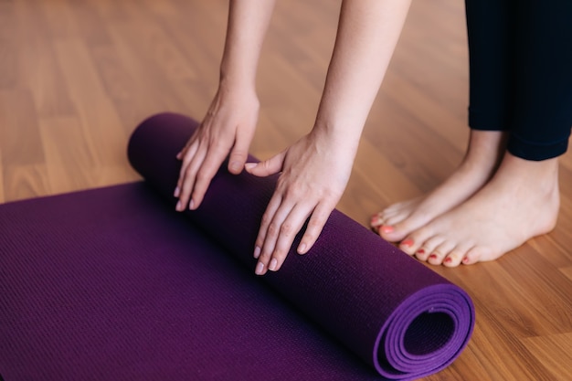 Close-up of girl folding fitness or yoga mat after working out at home in living room