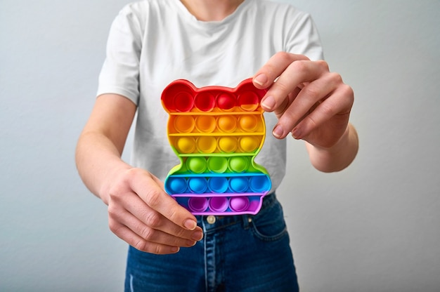 Close-up girl holding in hands colorful trendy pop it toy in form a bear.