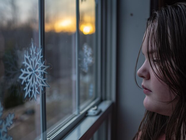 Foto close-up di una ragazza che guarda attraverso la finestra a casa