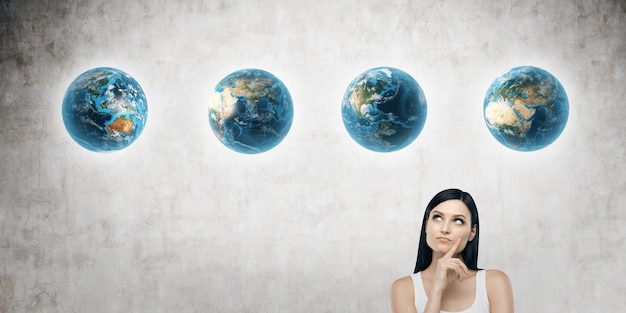 Close up of girl in tank top and four globes against concrete wall