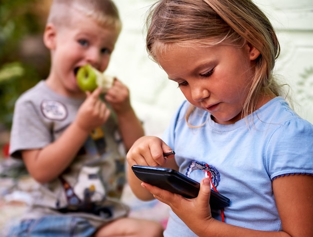 Foto close-up di una ragazza che usa il telefono mentre è seduta con il fratello fuori