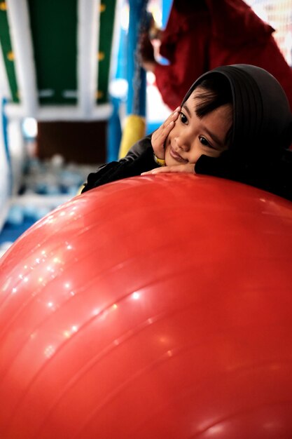 Close-up of girl wearing hijab leaning on red ball