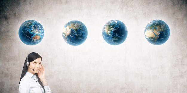 Close up of girl with headset and four globes against concrete wall