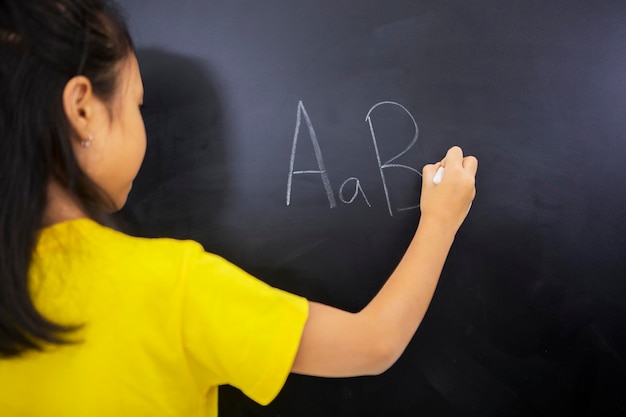 Close-up of girl writing on blackboard