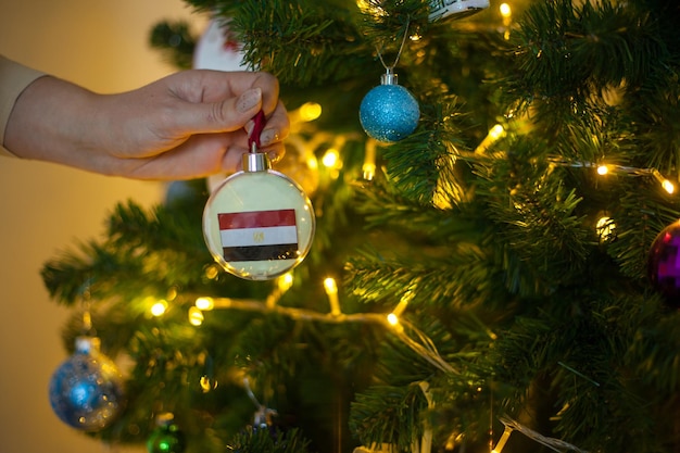 Primo piano della mano delle ragazze che tiene una palla di natale per un abete con la bandiera dell'egitto capodanno in egitto biglietto di auguri per le vacanze di capodanno con spazio per la copia del testo decorazione della casa per la celebrazione