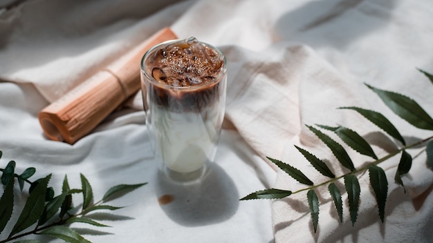 Close-up glas ijskoffie met melk op een witte doek met bladeren en schaduwen