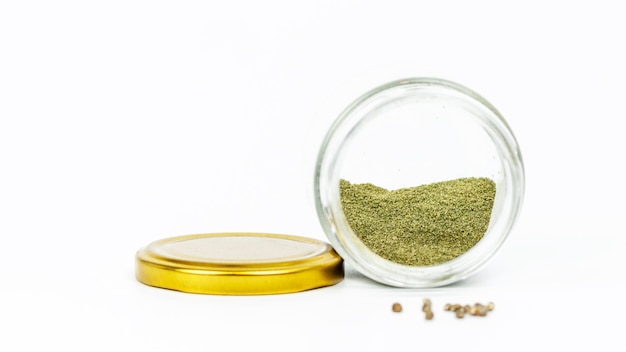 Close-up of glass jar with hashish and cannabis seeds on white.