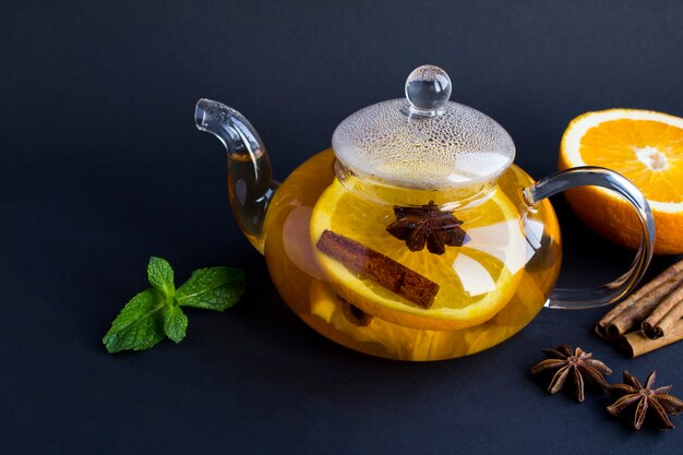 Close-up on glass teapot with orange, cinnamon and anise on the black  background. Copy space.