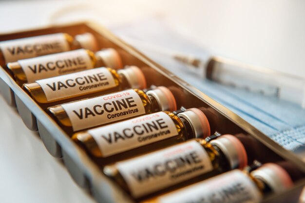 Close-up of glass vials with Covid-19 vaccine, medical mask, syringe. Scientific developments in the fight against viral infection, coronavirus, pulmonary pneumonia.