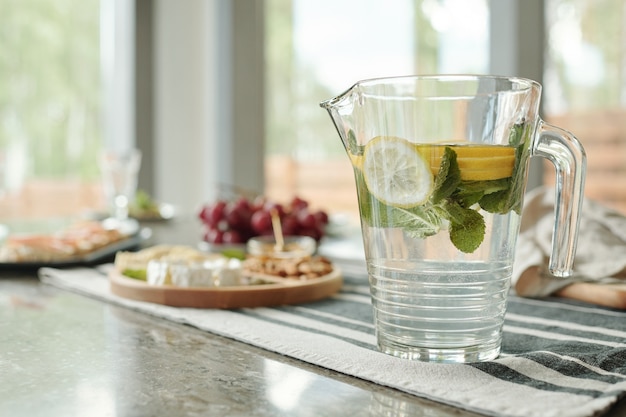 Primo piano della brocca vetrosa di limonata sul tovagliolo spogliato preparato per la cena a casa