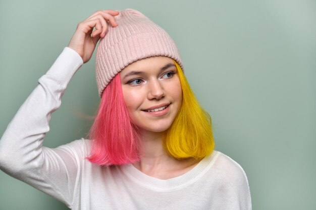 Close-up glimlachend vrouwelijk positief gezicht, portret van trendy tienermeisje met gekleurd geverfd haar, jonge hipster in hoed op groene pastelachtergrond, kopieer ruimte. Adolescentie, mode, haar, schoonheid