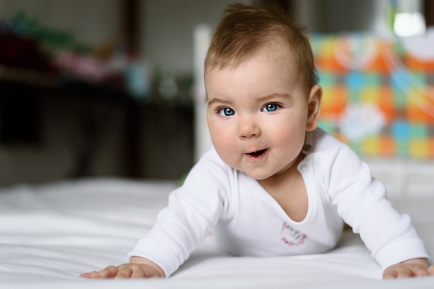 Foto close-up glimlachende blauwogige baby in witte romper op wit bed