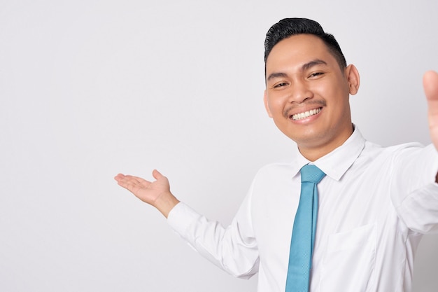Foto close-up glimlachende gelukkige leuke jonge aziatische zakenman met een formele hemd stropdas en het tonen van lege ruimte met hand geïsoleerd op witte achtergrond het nemen van een selfie op de telefoon