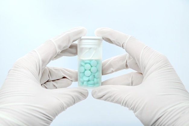 Close-up of gloved hands holding transparent pill bottle on white background. Concept: medication treatment, online ordering of medicines, contactless delivery of medicines