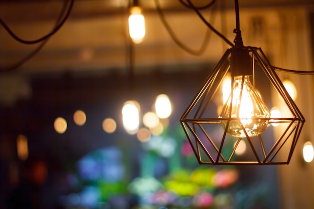 Close-up glowing hanging spherical retro vintage edison incandescent bulb against background of blurred other lamps