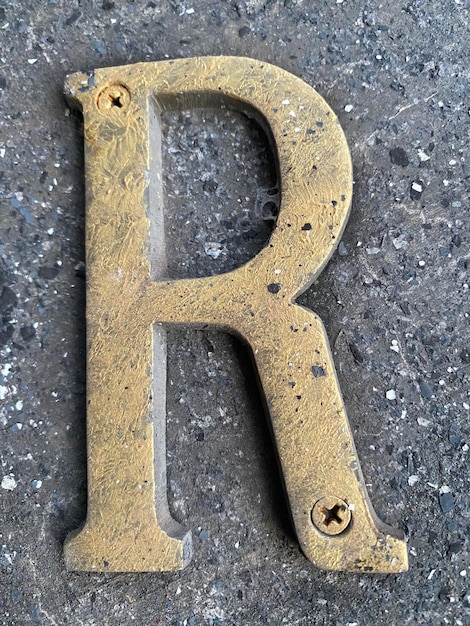 Photo a close up of a gold letter r on a concrete surface.