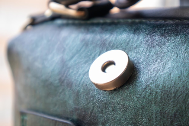 Close-up of gold magnetic button closure open elegant womens fashion green leather shoulder bag. Accessories, detail.