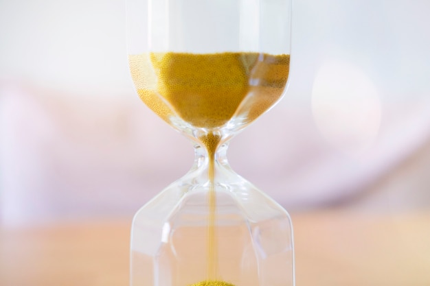 Close up gold sand running through the bulbs of an hourglass.
