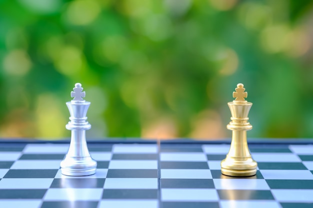 Close up of gold and silver King chess pieces on chessboard with green nature background