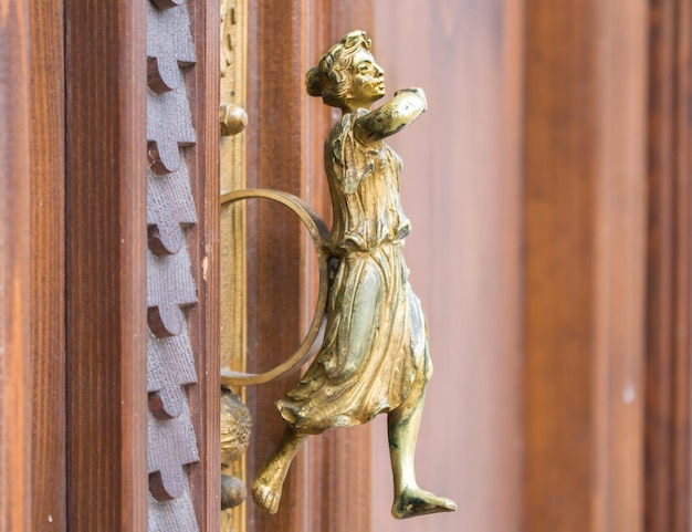 Close up golden door handle on the wooden door in the form of\
ancient rome women