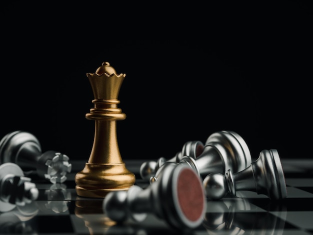 Close-up golden queen chess piece standing with falling silver pawn chess pieces on chessboard on dark background. Leadership, winner, competition, and business strategy concept.