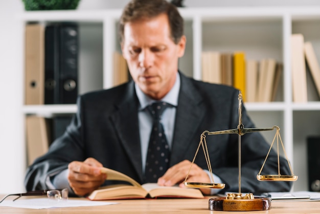 Close-up of golden scale in front of lawyer reading book in the courtroom