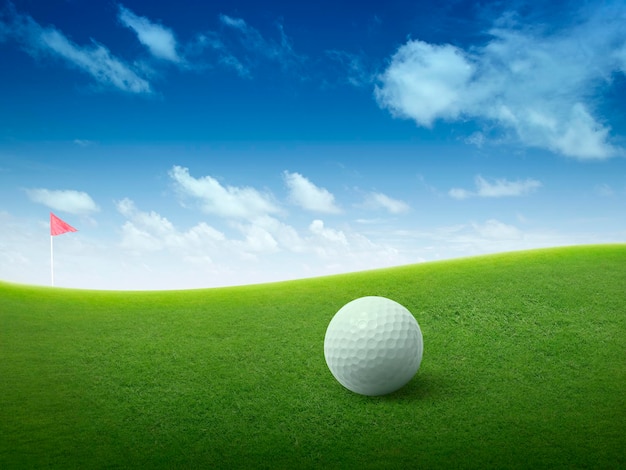 Close up golf ball on green grass field and red golf flag on green fairway with beautiful blue sky