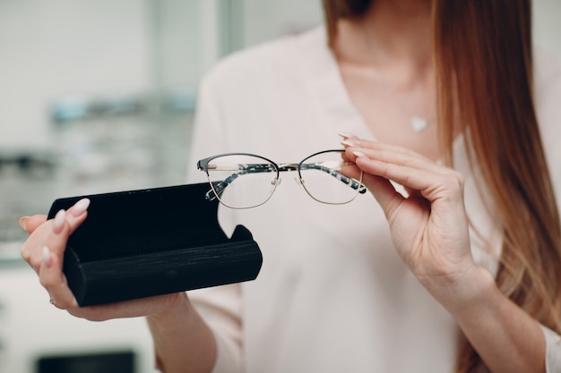 Primo piano di una splendida giovane donna sorridente che sorride raccogliendo e scegliendo gli occhiali all'angolo dell'ottico al centro commerciale. felice bella donna che compra occhiali da vista dall'optometrista