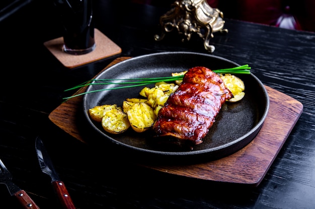 Close up Gourmet Main Dish with Grilled Pork Rib and Fried Potatoes on Black pan. Served on Wooden Board