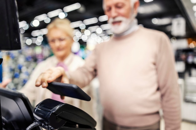 Close up of grandfather using smart phone for checkout on selfservice cash register in supermarket