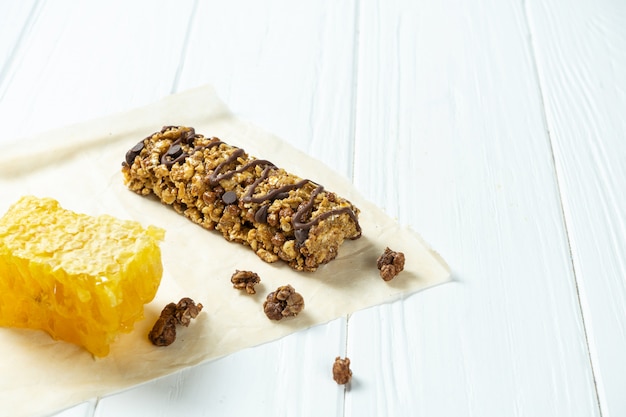 Close up on Granola Bar with honeycombs on craft paper on white wooden background.
