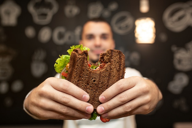 Close-up grappig vaag portret van jonge mensengreep gebeten sandwich door zijn twee handen.