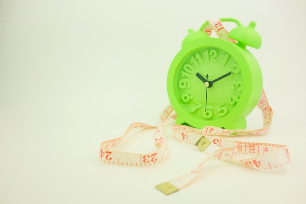 close-up of green alarm clock with tape measure against gray background
