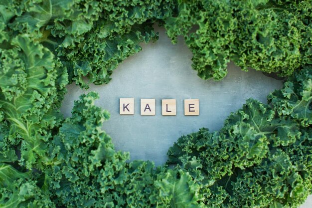 Close up of green curly kale salad and wooden scrabble letters on a grey concrete background