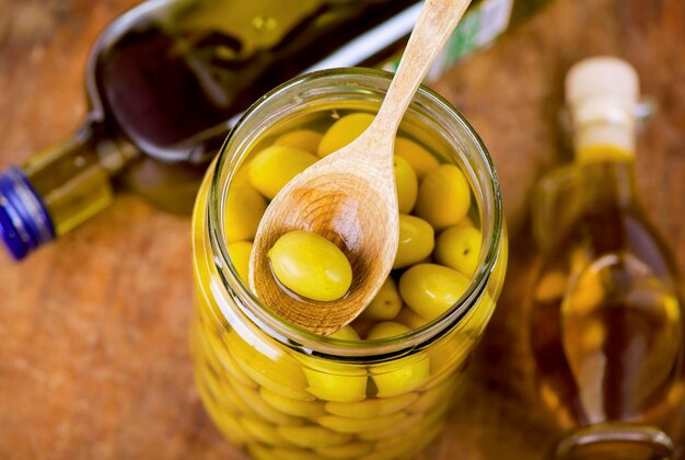 Close up green olives in bank bottle of olive oil rosemary on a wooden background