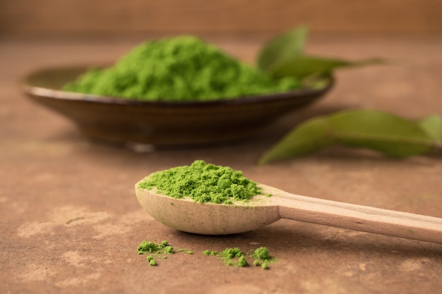 Foto chiuda in su della polvere del tè verde in cucchiaio di legno sulla tabella.