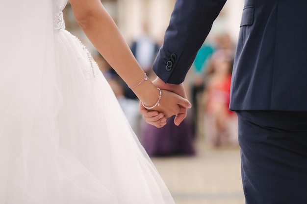 Close up of groom hold brides hand in front of guests wedding ceremony back view