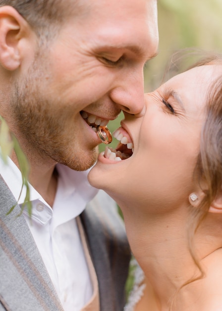 Крупным планом жених держит кольцо в зубах, и невеста смеется