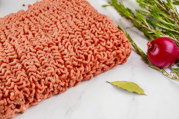 Close up of ground beef with onion, rosemary and bay leaf on white background.