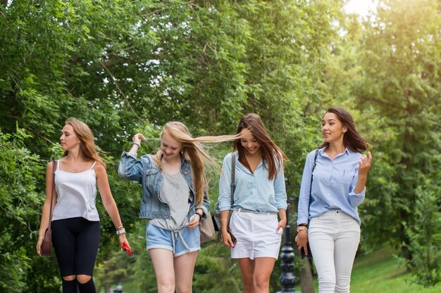 Close up of group of four girlfriends going home after walking together at park. female students walking after study and having fun