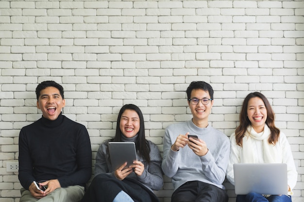 close up group of millennial generation holding modern gadget devices and sitting on white wall room