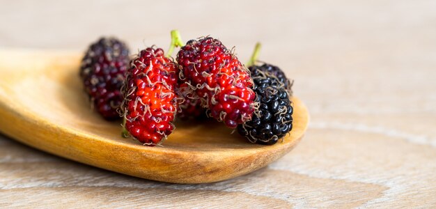 Close up group of mulberries is placed on a wooden spoon on a wooden table.