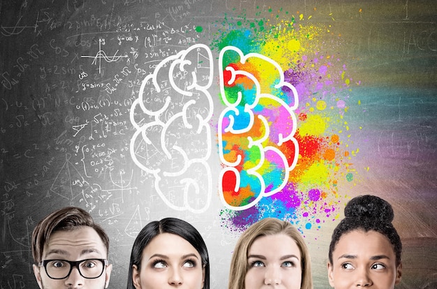 Close up of a group of young business people standing near a blackboard with a brain and color splashes combined with formulas.