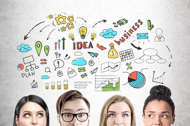 Close up of a group of young business people standing near a concrete wall with a colorful business idea sketch drawn on it.